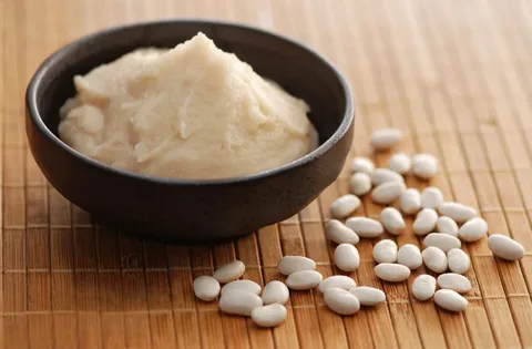 A bowl of white bean paste with scattered white beans on a wooden surface.