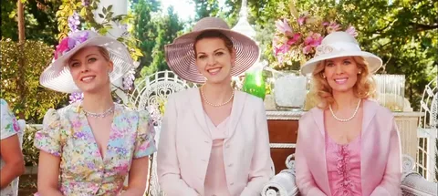 A woman wearing a pink hat and light pink outfit smiles at an outdoor event.