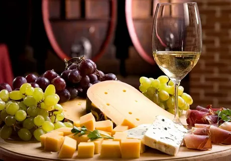Cheese platter with grapes and wine glass in front of barrels.