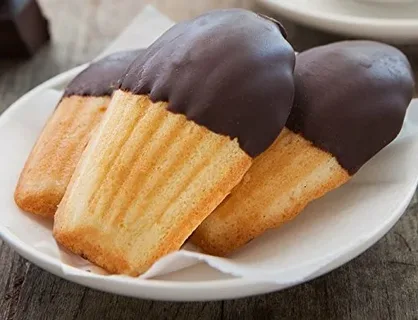Madeleines dipped in chocolate on a white plate.