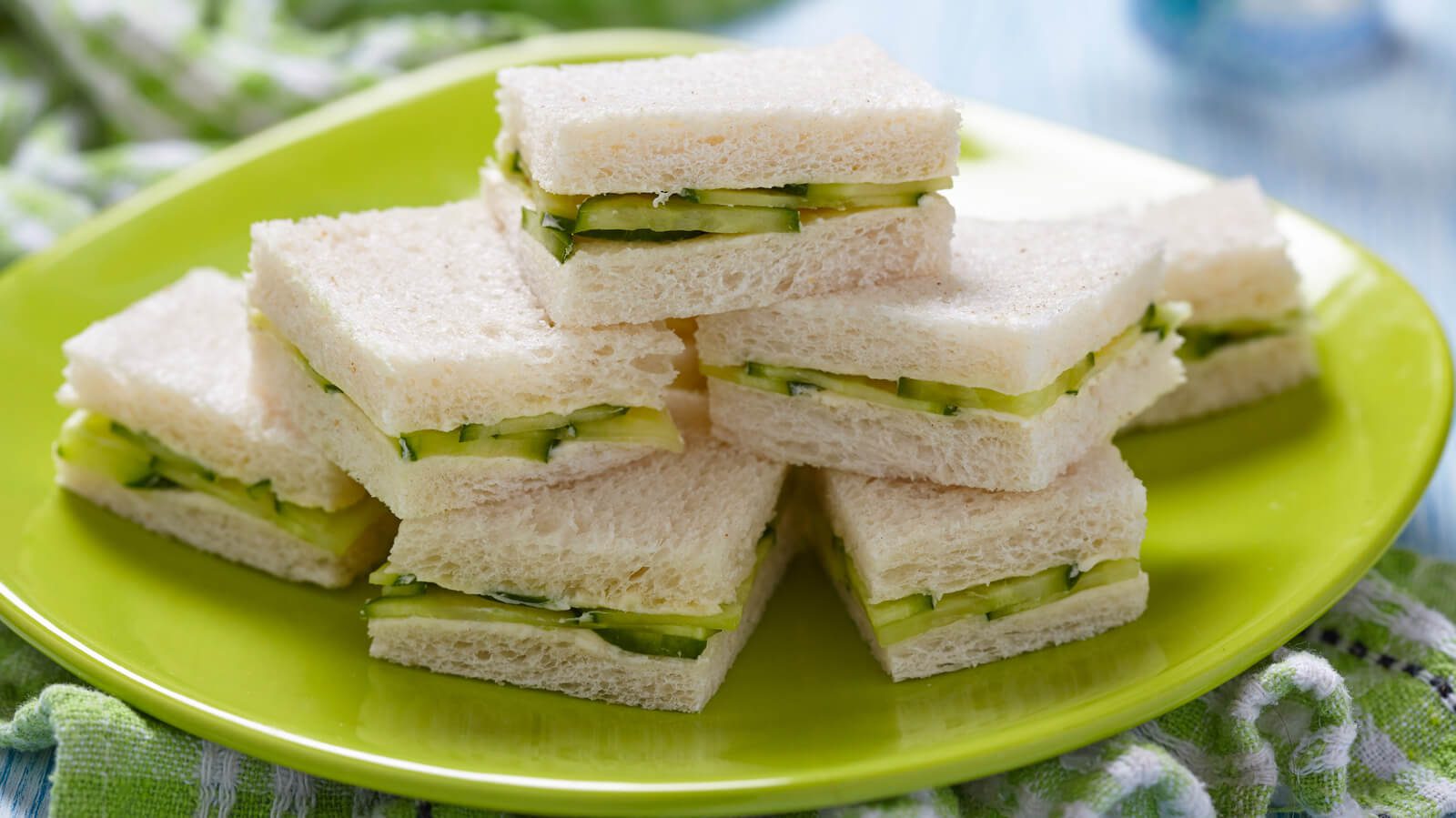 Stack of cucumber tea sandwiches on a green plate.