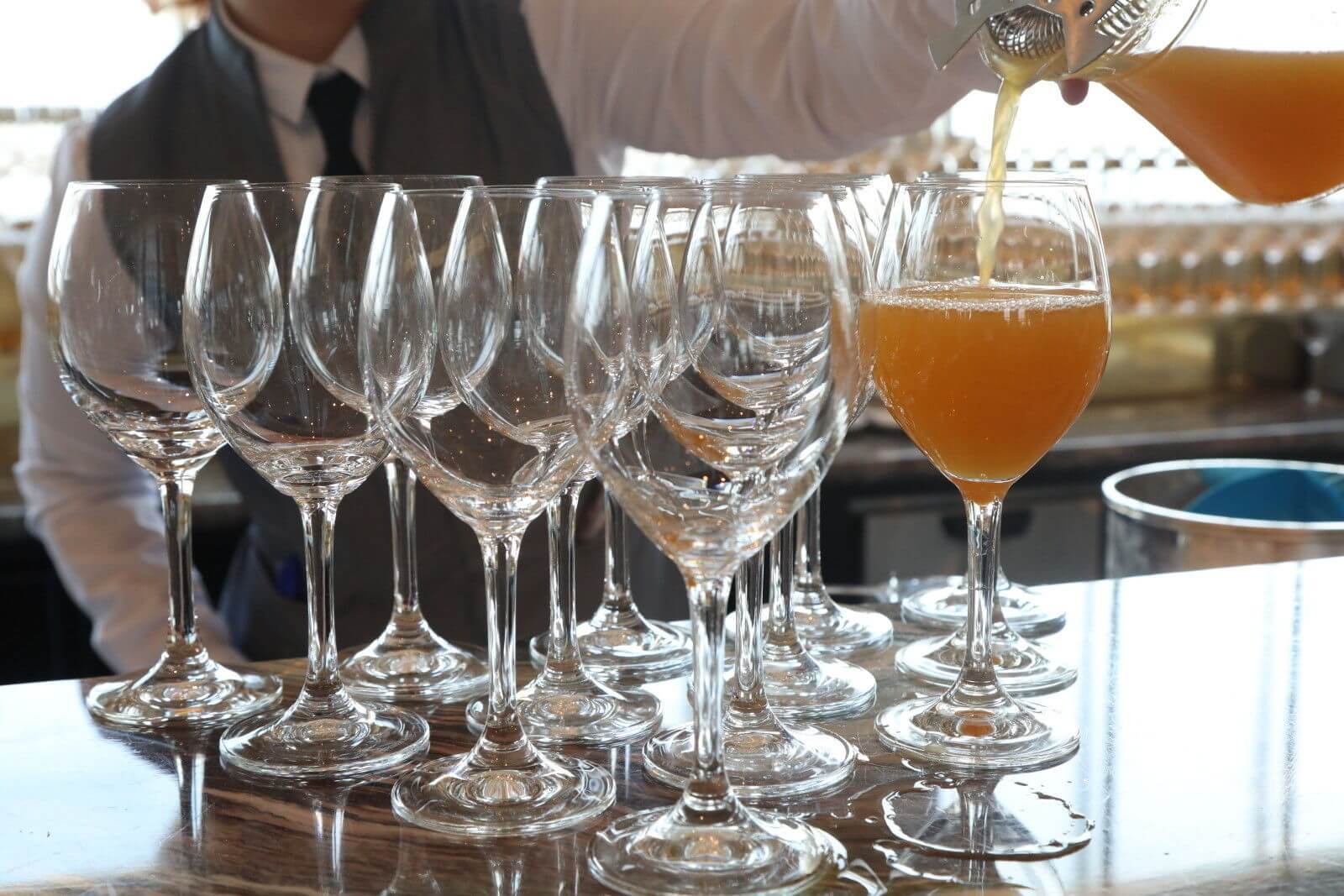 Row of empty wine glasses with one being filled with orange juice.