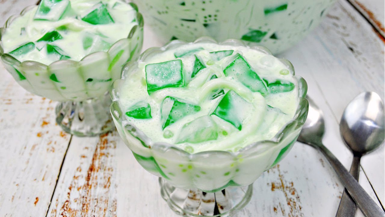 A dessert bowl filled with green jelly cubes in creamy white sauce.