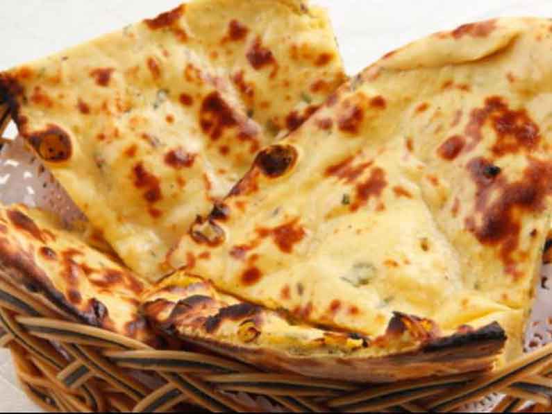 Basket of freshly baked naan bread with golden spots.