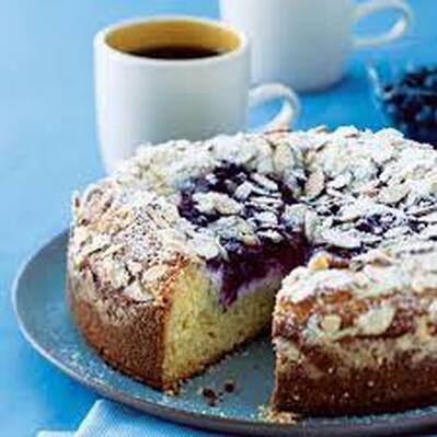 A sliced almond cake on a blue plate with a cup of coffee in the background.