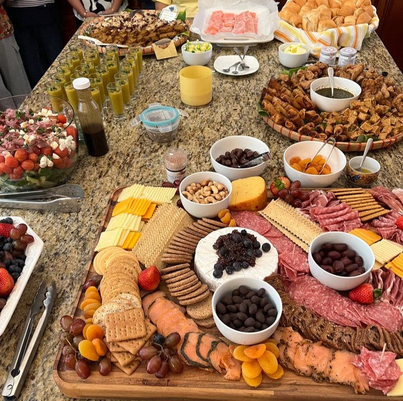 A charcuterie board with meats, cheeses, nuts, and dips on a table with snacks.