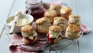 Freshly baked scones with cream and jam on a cooling rack.