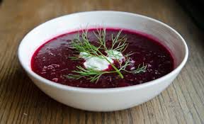 Bowl of vibrant beet soup garnished with cream and dill.