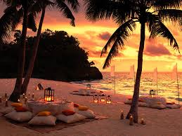 Romantic beach setup at sunset with candles and cushions.