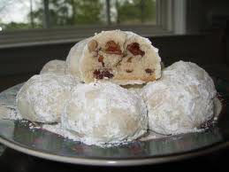 Powdered sugar-covered cookies with a fruit and nut filling on a plate.