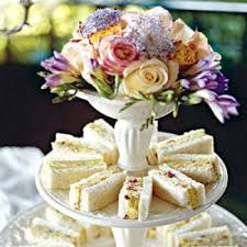 Elegant tiered stand with assorted floral bouquet and cream-filled sandwiches.
