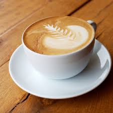 A latte with leaf-shaped foam art in a white cup on a wooden table.