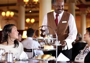 A waiter serves afternoon tea to a smiling woman in a cozy restaurant.