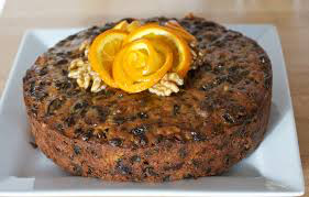 A round fruitcake decorated with an orange peel rose and walnuts on top.