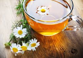 A cup of chamomile tea with fresh chamomile flowers on a wooden table.