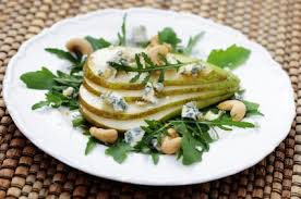 Baked pear with blue cheese, arugula, and nuts on a white plate.