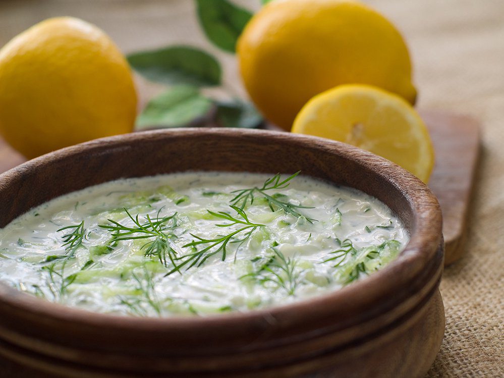A bowl of creamy dill sauce with fresh lemons in the background.