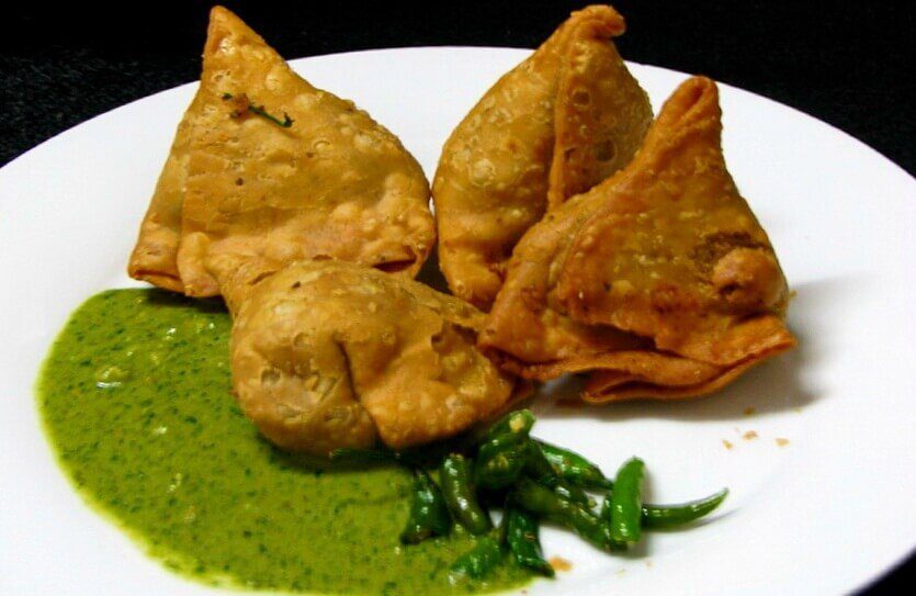 Crispy samosas served with green chutney and fried green chilies.