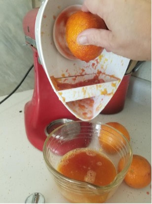 A juicer extracting orange juice into a glass bowl.