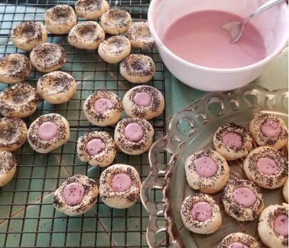 Mini tartlets with pink icing and decorative centers on cooling racks.