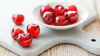 Fresh red cherries on a white surface with a bowl in the background.