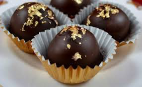 Close-up of chocolate truffles with nuts on top in gold wrappers.