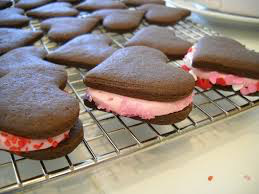Heart-shaped chocolate cookies with pink filling cooling on a rack.