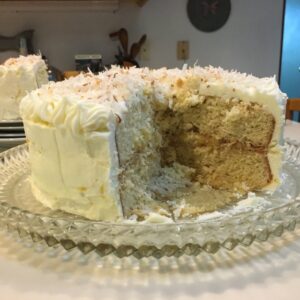 A partly eaten layered cake with white frosting on a glass plate.