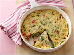 A vegetable frittata with a slice removed in a white dish.