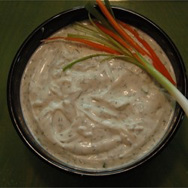 A bowl of creamy dip garnished with green onions and carrot sticks.