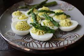 Deviled eggs garnished with fresh asparagus tips on a decorative plate.