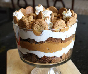 Layered pumpkin dessert with whipped cream and cookies in a glass bowl.