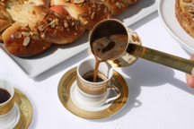 Pouring coffee into a small cup with pastries in the background.