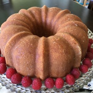 A bundt cake surrounded by fresh raspberries on a glass plate.