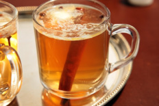 A glass mug of hot spiced tea with a cinnamon stick.