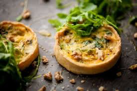 Two savory mini quiches garnished with fresh greens on a rustic surface.