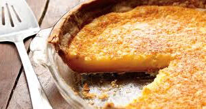 A slice of pumpkin pie in a dish with a golden crust.