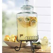 Glass dispenser with lemon-infused water and slices on a stand.