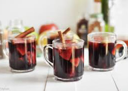 Three glass mugs filled with mulled wine garnished with cinnamon sticks and orange slices.