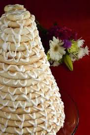 A close-up of a decorated layered cake with white icing and flowers in the background.
