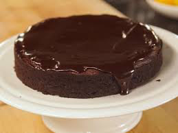 A rich chocolate cake with glossy ganache on a white stand.