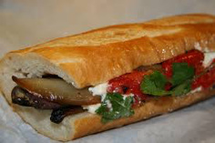 Close-up of a sandwich with eggplant, greens, and red pepper on a baguette.