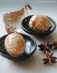 Tea eggs with cracked marbled shells in black bowls, accompanied by star anise.