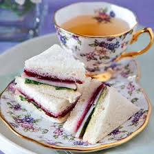 Elegant tea cup with layered finger sandwiches on matching floral plate.