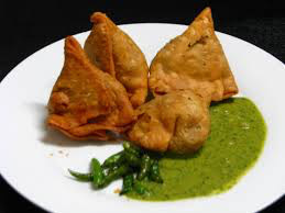 Plate of Indian snacks including samosas and chutney.