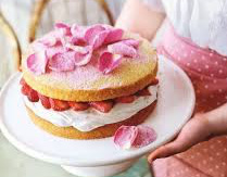 A small cake with strawberries and pink rose petals on top.