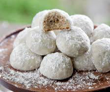 Powdered sugar-coated cookie balls with a nutty center on a wooden plate.