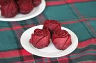 Three red rose-shaped desserts on a white plate.