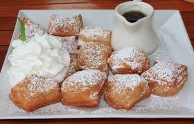 Beignets dusted with powdered sugar, served with whipped cream and coffee.