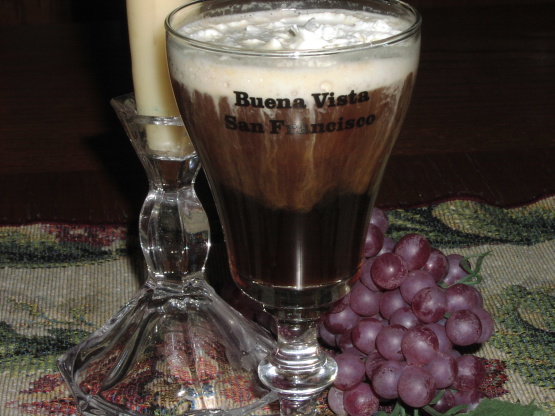 A layered coffee drink in a glass with grapes and a candle beside it.